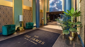 A hotel lobby with a large carpet reading "The James Hotel, Amsterdam" and a large wall mural of clouds.