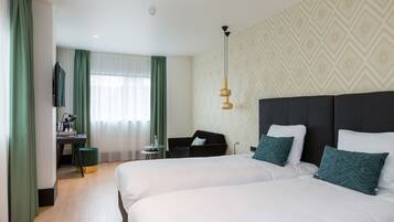 A hotel room with two beds, a desk, a chair, and a TV.