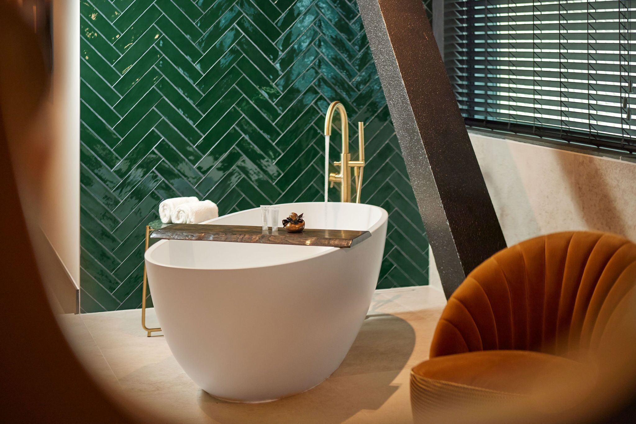 Un baño moderno con una bañera independiente, un grifo dorado y una pared con motivo de espiga verde.