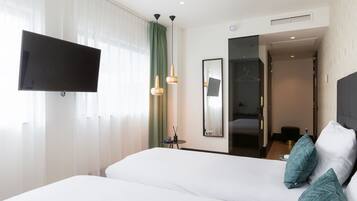 A hotel room with a large bed, a flat-screen TV mounted on the wall, a small table with a phone and a candle, and a mirror on the wall.