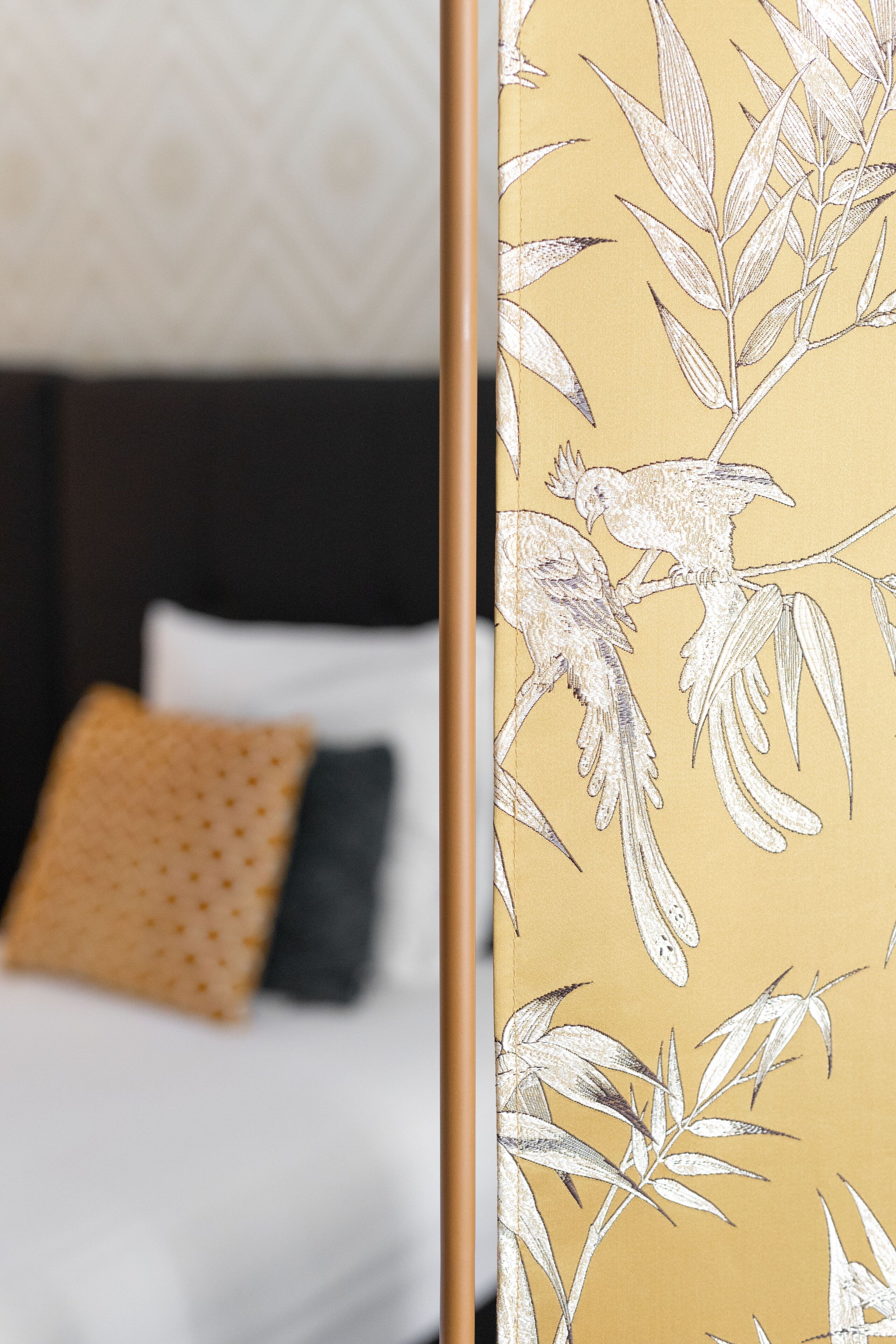 Una cama con almohadas blancas y negras, una pared amarilla con diseño y un papel tapiz con motivos florales.