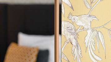 Una cama con almohadas blancas y negras, una pared amarilla con diseño y un papel tapiz con motivos florales.