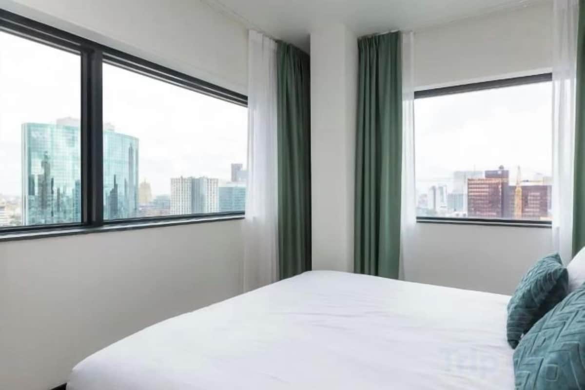 Une chambre d’hôtel avec un lit, deux fenêtres et une vue sur le paysage urbain.