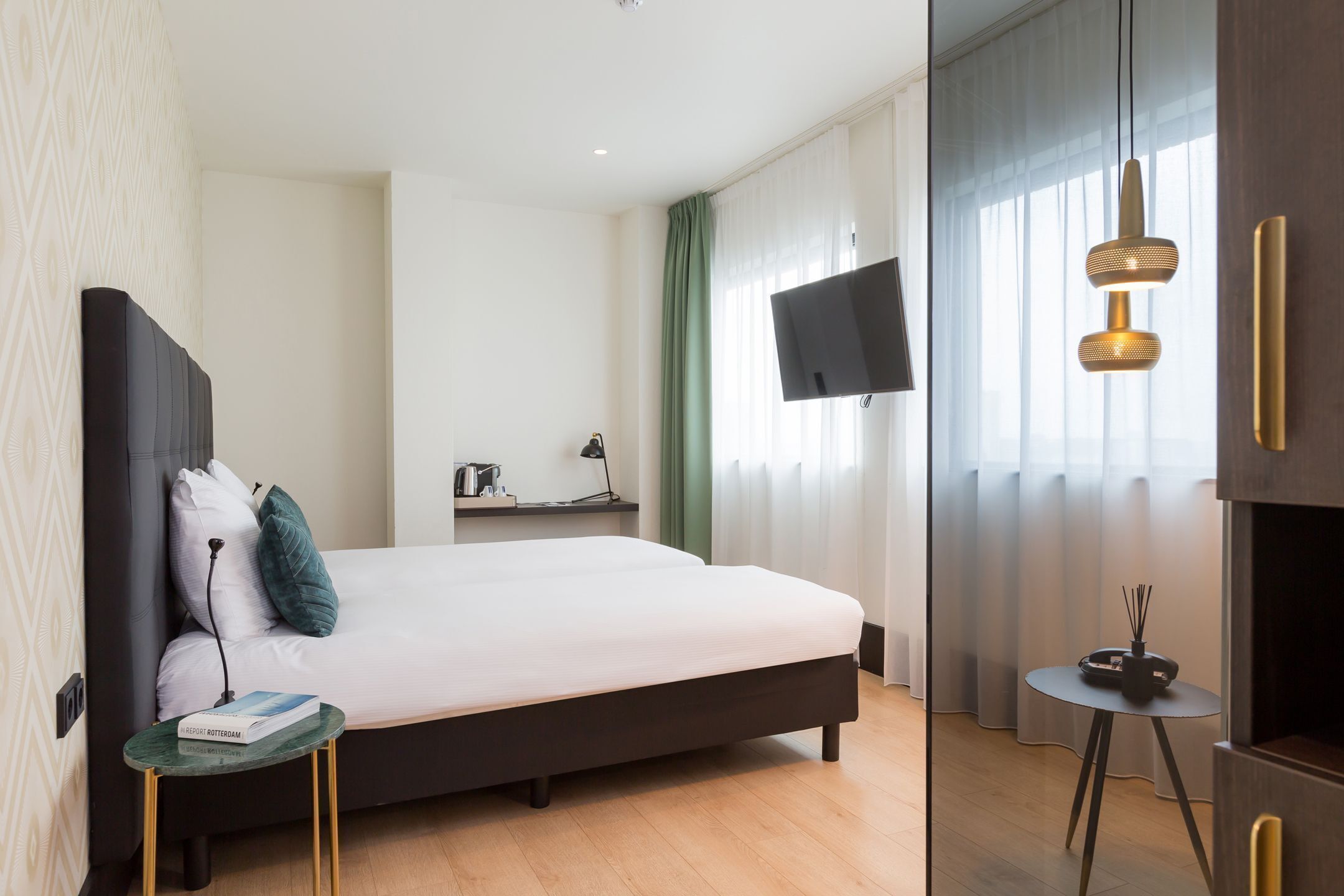 A modern hotel room with a large bed, a TV, a small table with a book, and a decorative light fixture.