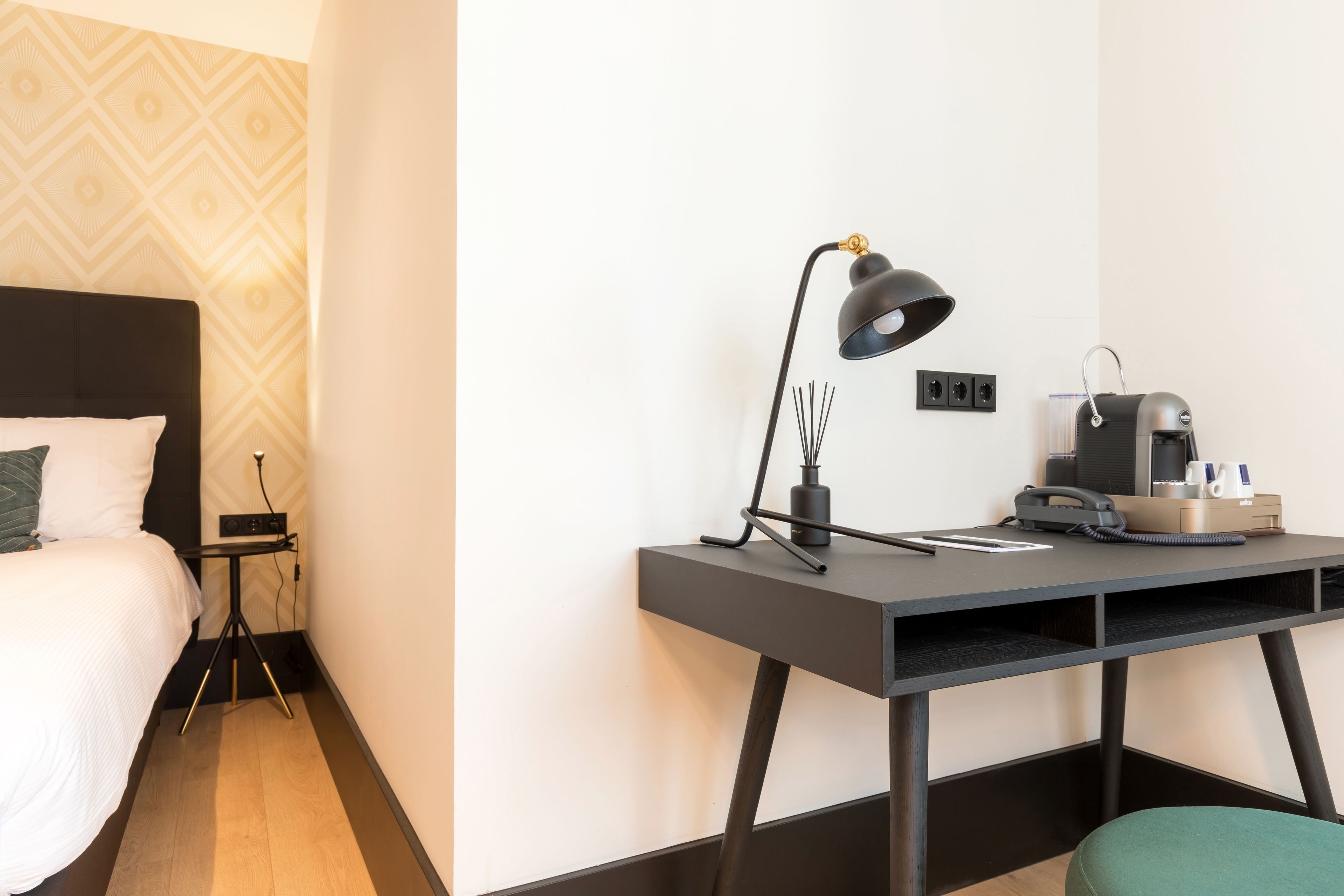 A hotel room with a bed, a desk with a lamp, a phone, and a coffee maker.