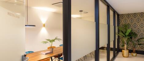 A modern meeting room with a wooden table, orange chairs, and potted plants.