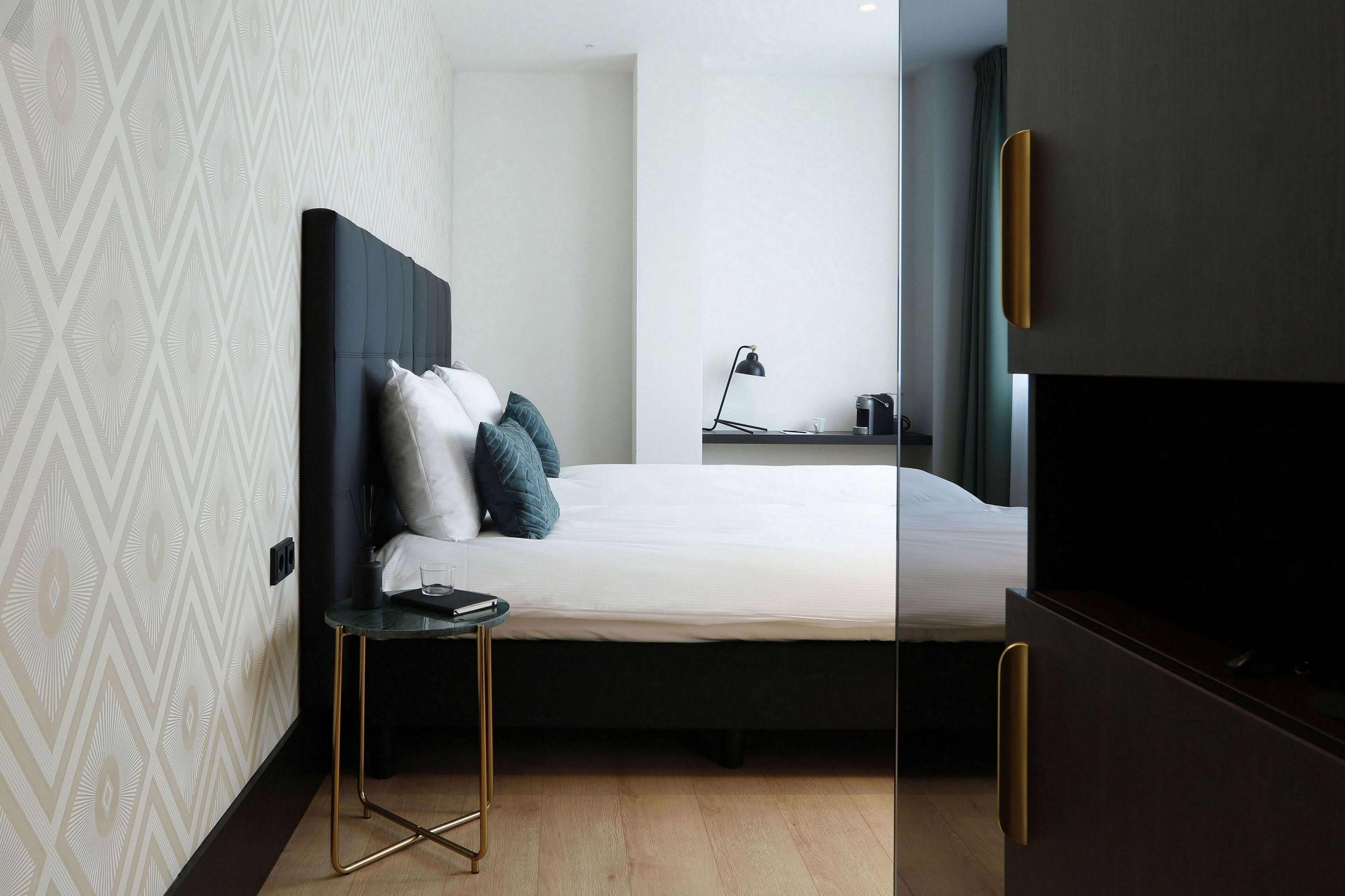 A modern hotel room with a large bed, a bedside table, a lamp, and a TV.