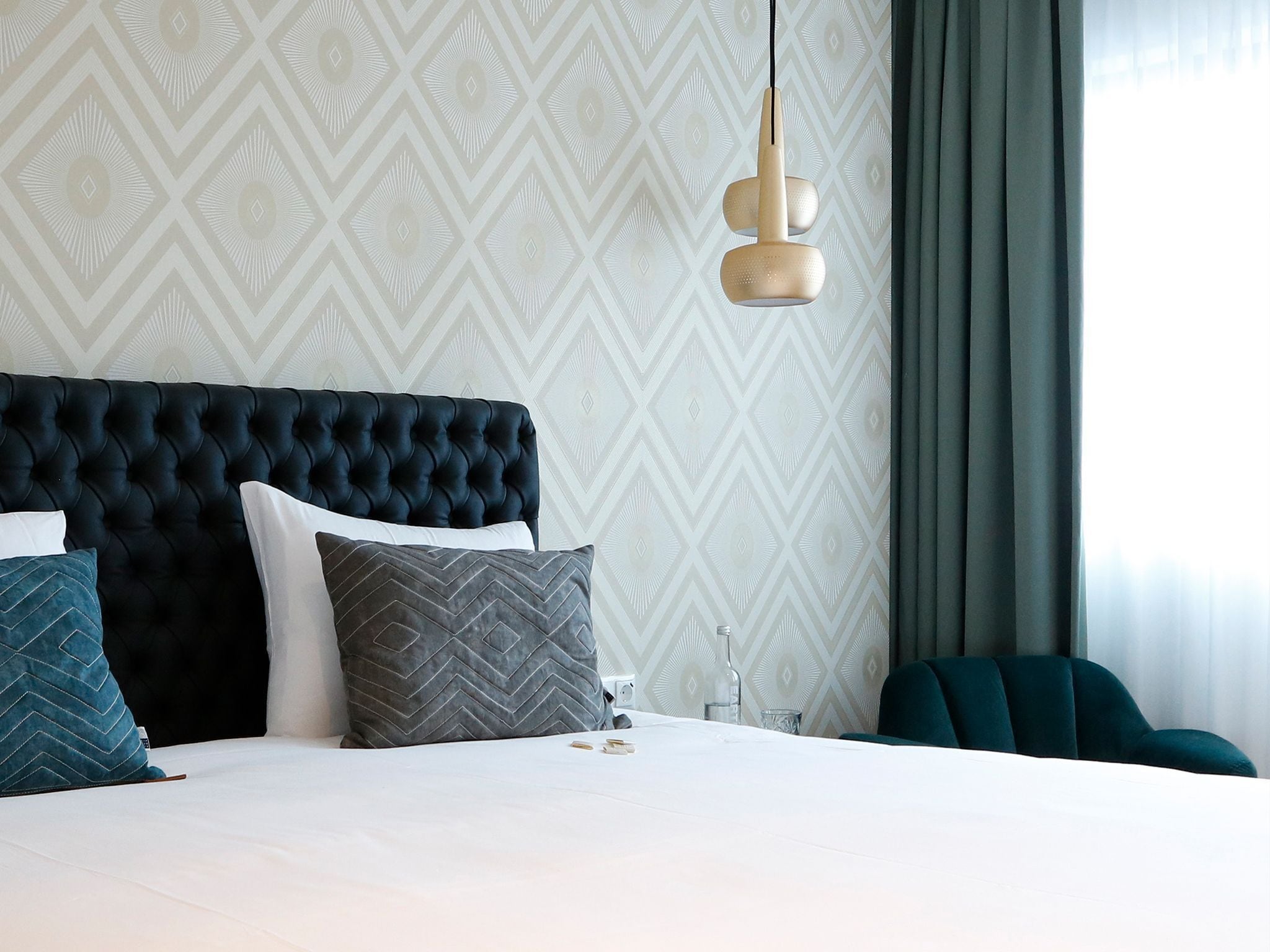 Una moderna camera d'albergo con una testiera trapuntata, un letto grande e una lampada a sospensione.