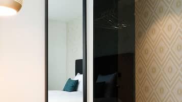 Una habitación de hotel moderna con un espejo grande, un otoman verde y una cama con marco negro.