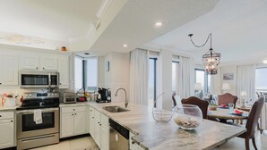 A modern kitchen with stainless steel appliances, a dining area with a chandelier, and large windows. - 501W - Contemporary 3BR Beachfront Condo! (Orange Beach)