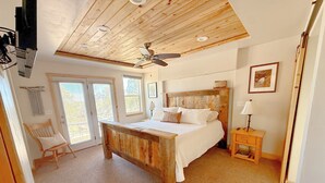 A bedroom with a wooden bed, a ceiling fan, a nightstand, a chair, and a window. - The Cedars Country Cottage (Blanding)