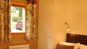Ein Schlafzimmer mit Bett, einem Fenster mit Vorhängen, einer Wandlampe und einer Deckenleuchte.