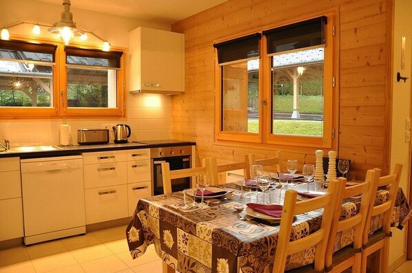 A cozy kitchen with wooden cabinets, a dining table set for four, and a window overlooking a garden.