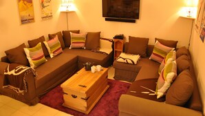 Ein gemütliches Wohnzimmer mit einem Ecksofa, einem Holztisch und einem an der Wand befestigten Fernseher.