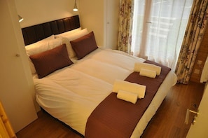 A neatly made bed with white and brown linens, a headboard, and two bedside lamps.