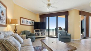 Sala de estar com sofá, poltronas, mesa de centro, televisão e varanda com vista.