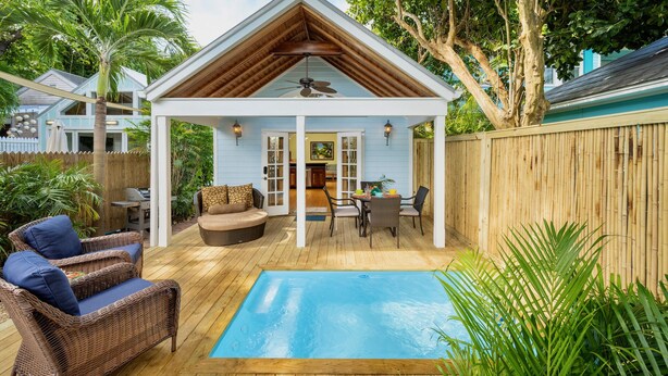 Uma área de estar coberta ao ar livre, com piscina, mobiliário de vime e um deck de madeira.