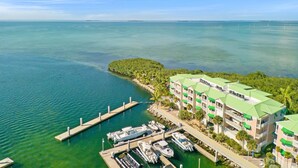 A coastal hotel with multiple green-roofed buildings, a marina with several boats, and a small island with dense vegetation. - **SUNSET POINT @ SUNSET MARINA** Condo / Pool + Last Key White Glove Service... (Key West)