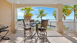 A covered outdoor patio with a table and chairs, overlooking a body of water and palm trees. - **SUNSET POINT @ SUNSET MARINA** Condo / Pool + Last Key White Glove Service... (Key West)