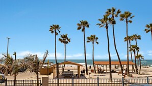 Una playa con palmeras, una zona de estar cubierta y un puesto de salvavidas.