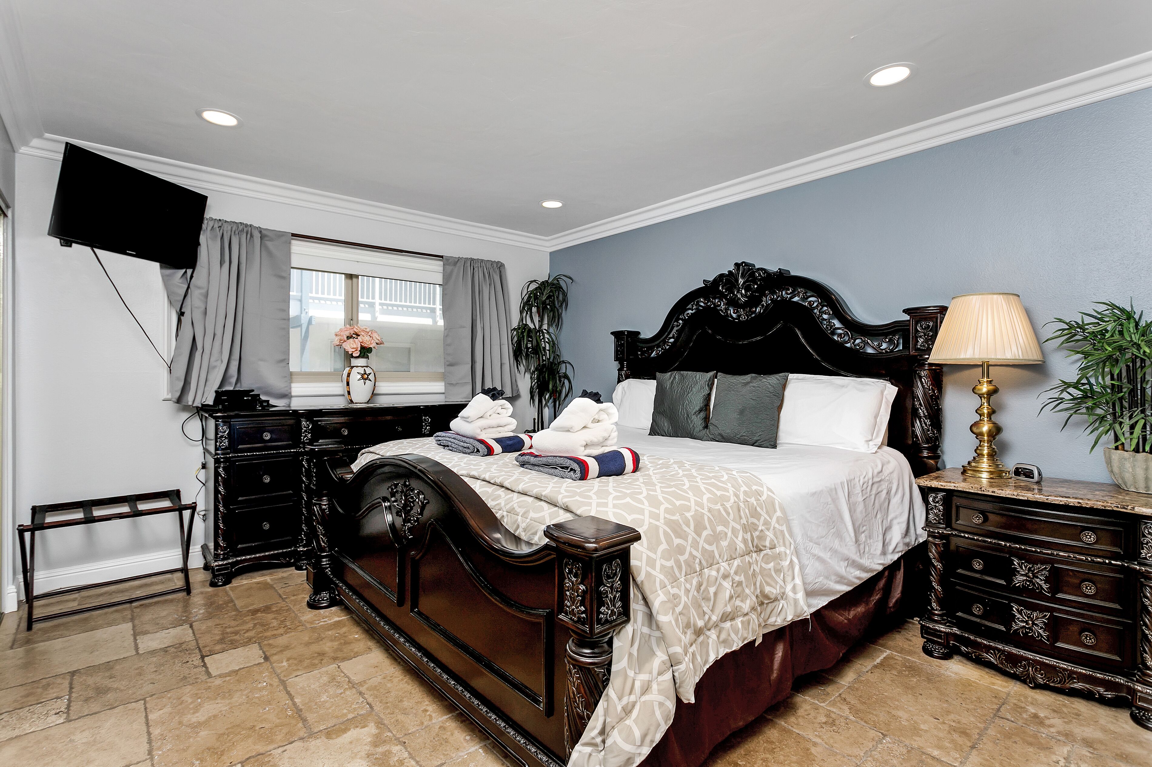 Une chambre à coucher avec un grand lit, des meubles en bois foncé, un téléviseur à écran plat et une fenêtre avec des rideaux.