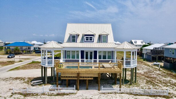 A beachfront house with a covered porch, multiple windows, and a deck.