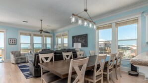 A spacious dining area with a large wooden table and chairs, a ceiling fan, and a view of the ocean through large windows.