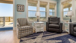A living room with a patterned armchair, a leather sofa, and a blue and white striped rug. There are two white nightstands with lamps, and a framed picture on the wall.