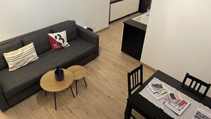 Un soggiorno moderno con un divano grigio, due tavolini piccoli e un tavolo da pranzo con riviste.