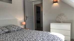 Una camera da letto con una coperta dal disegno decorativo, una lampada da comodino, un comò bianco e un punto luce a parete.