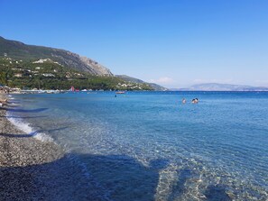 A clear beach with pebbles, calm water, and a distant mountain. - Villa Valia Seaside (Exclusive beach access Villa-Ipsos bay Corfu) (Ipsos)