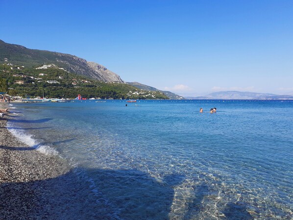 A clear beach with pebbles, calm water, and a distant mountain. - Villa Valia Seaside (Exclusive beach access Villa-Ipsos bay Corfu) (Ipsos)