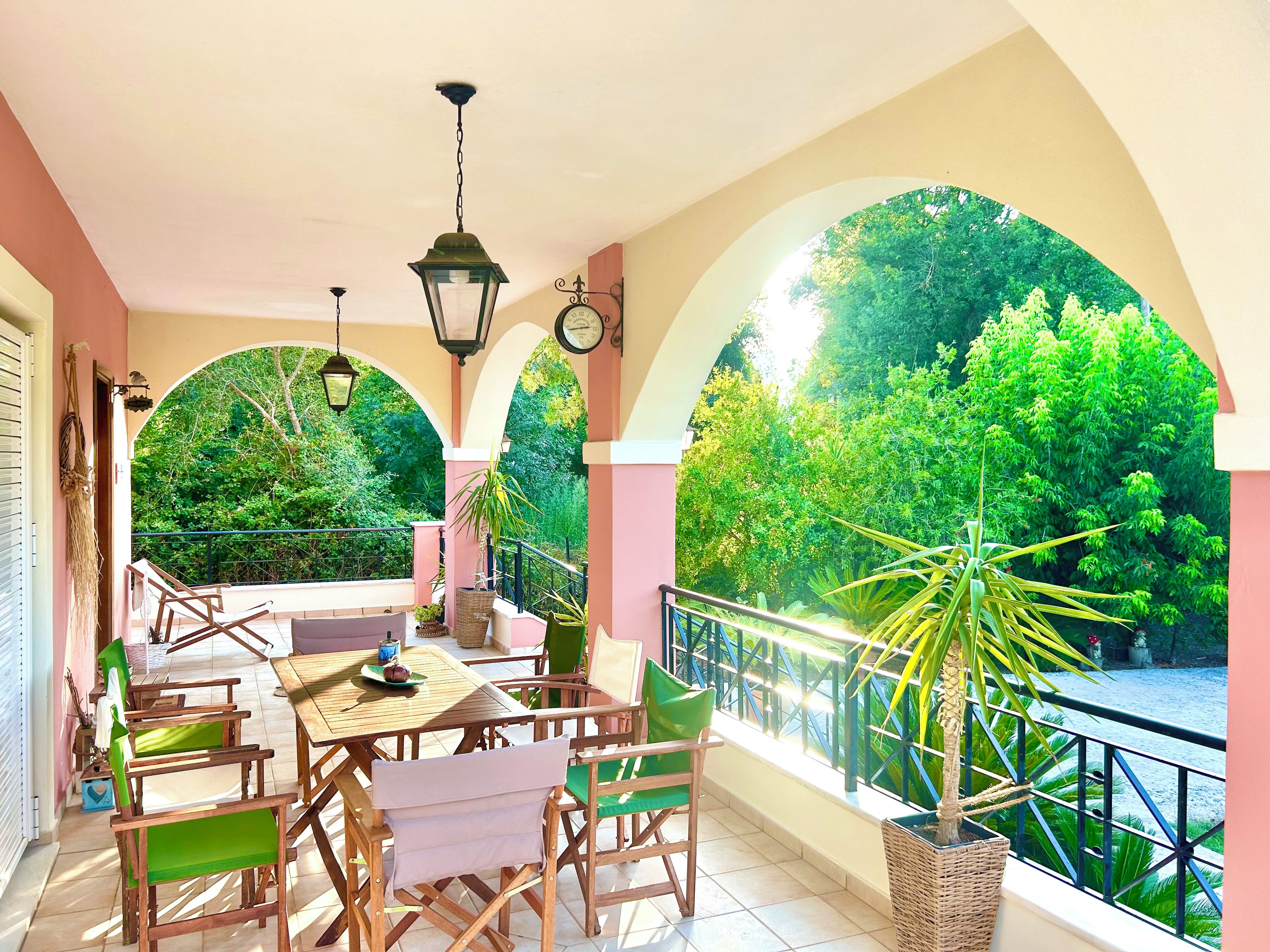 A balcony with a table and chairs, a hanging lantern, and a view of lush greenery.
