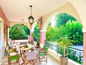 A balcony with a table and chairs, a hanging lantern, and a view of lush greenery. - Villa Valia Seaside (Exclusive beach access Villa-Ipsos bay Corfu) (Ipsos)