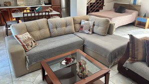 A living room with a sectional sofa, a glass coffee table, and a bed with a headboard.