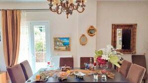 A dining room with a table set for four, surrounded by chairs, a chandelier, and a painting on the wall.