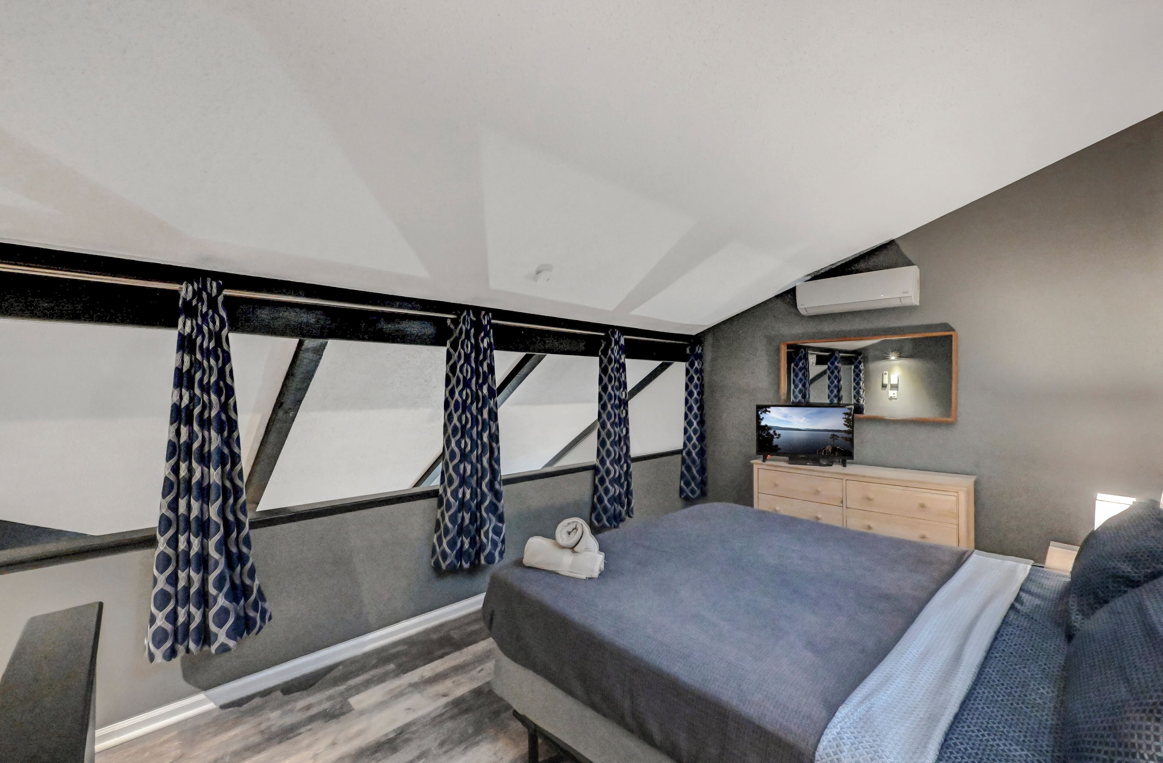 A bedroom with a bed, a dresser, a mirror, and patterned curtains.