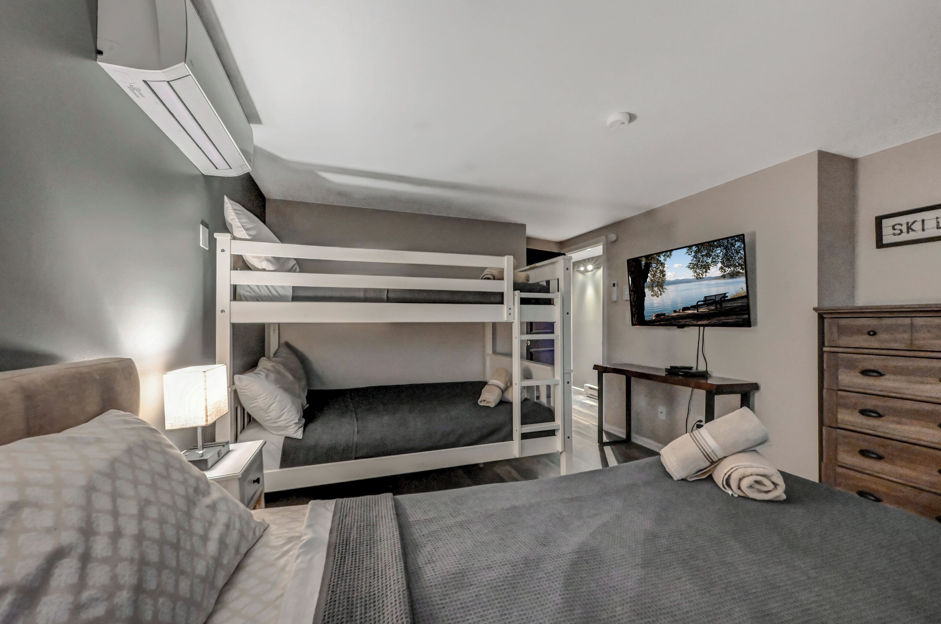 Ein Hotelzimmer mit Etagenbett, Schreibtisch mit Stuhl, Fernseher, Kommode und einem Bild an der Wand.