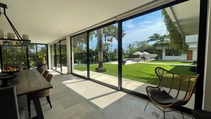 Ein modernes Interieur mit einer großen Schiebeglastür, die zu einem gepflegten Außenbereich mit Rasen, Sitzgelegenheiten und einem Pool führt.