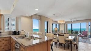 A modern kitchen with a large island, dining area with chairs, and a view of the ocean. - Sensational Gulf Front Views and Pristine White Quartz Beaches (Orange Beach)