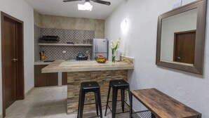 Cocina compacta con una isla central, dos taburetes, una mesita y un ventilador de techo.