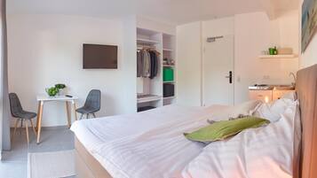 A hotel room with a bed, a desk with two chairs, a TV, a closet, and a small kitchenette.