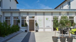 Una entrada de edificio con un letrero de bienvenida, plantas en macetas y asientos al aire libre.