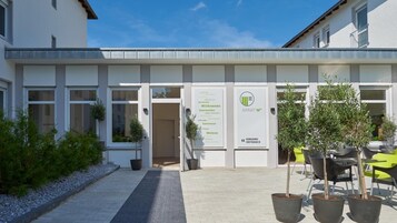 Una entrada de edificio con un letrero de bienvenida, plantas en macetas y asientos al aire libre.