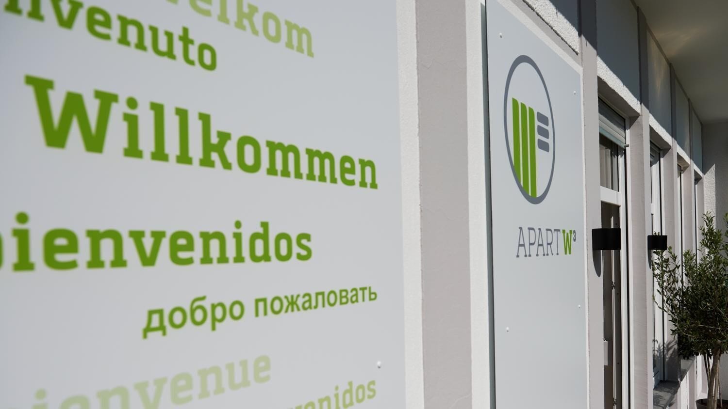 A welcome sign with multilingual greetings and a logo for 'APART W'.
