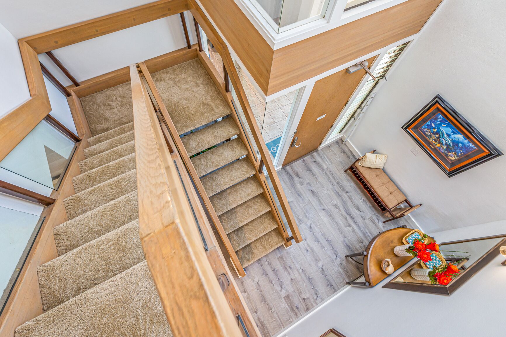 A multi-level interior with a wooden staircase, a small seating area with a table and chairs, and a framed picture on the wall.