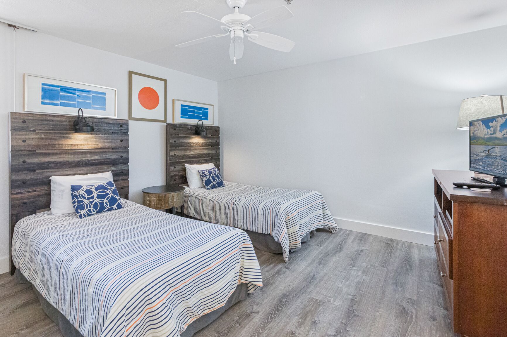 A hotel room with two beds, a desk, and a ceiling fan.