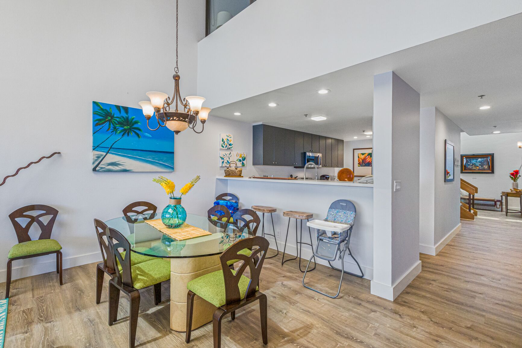 A modern kitchen with a dining area, featuring a glass table, wooden chairs, and a hanging light fixture.