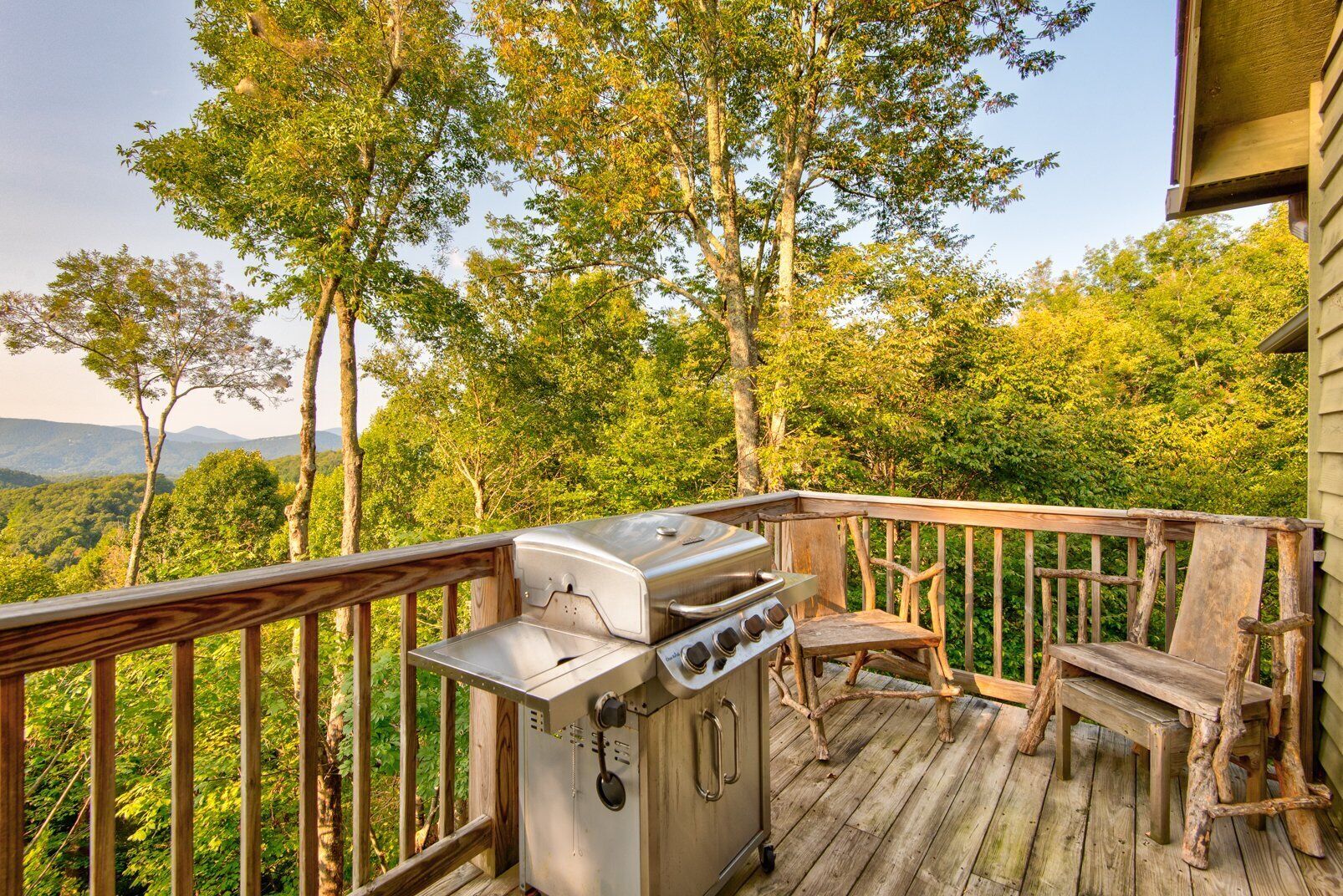 A deck with a stainless steel grill, a wooden bench, and a view of a forested landscape.