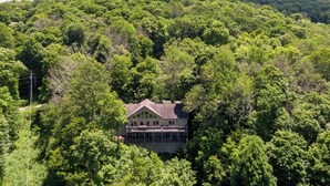 Ein Haus, umgeben von dichtem Wald, mit einem markanten Balkon und freiem Blick zum Himmel.